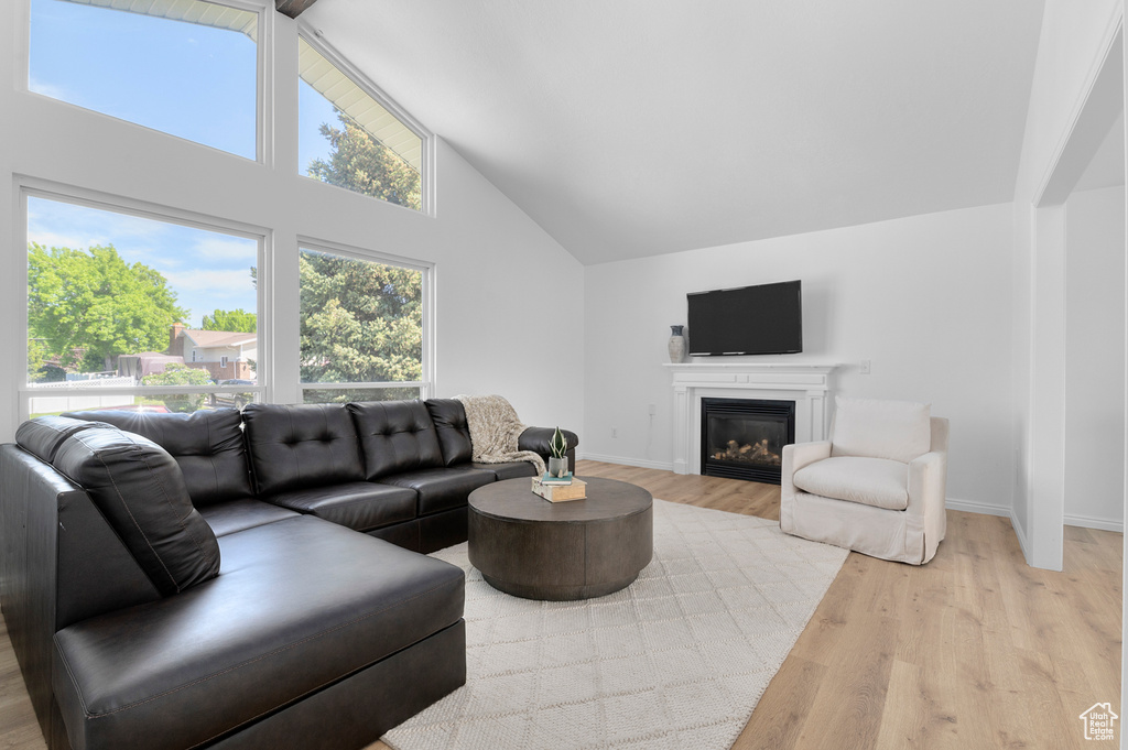 Living room featuring light wood-style flooring, high vaulted ceiling, baseboards, and a glass covered fireplace