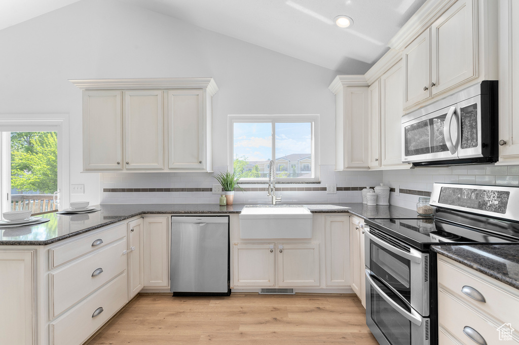 Kitchen featuring stainless steel appliances, vaulted ceiling, a peninsula, backsplash, and a sink