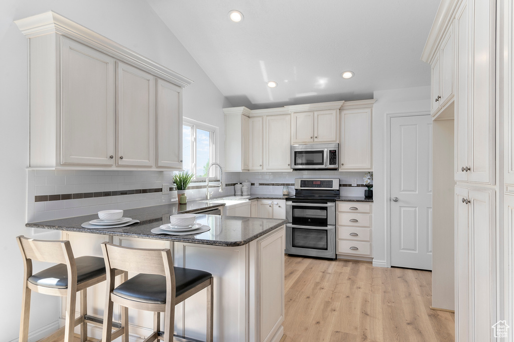 Kitchen featuring stainless steel appliances, a peninsula, lofted ceiling, tasteful backsplash, and dark stone countertops