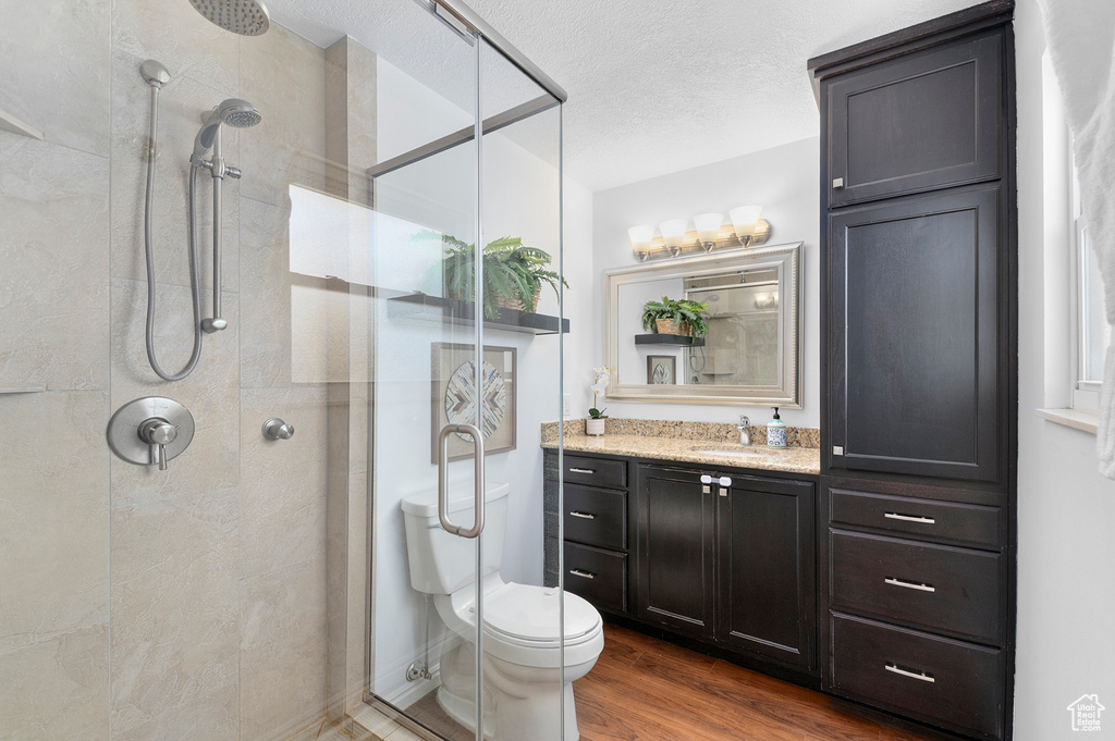 Full bathroom with a stall shower, wood finished floors, vanity, toilet, and a textured ceiling