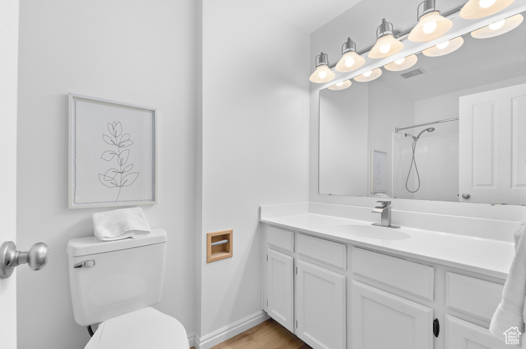 Full bathroom with toilet, vanity, a shower, wood finished floors, and baseboards
