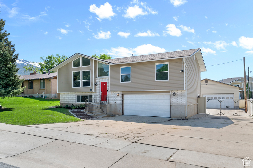 Raised ranch featuring brick siding, an attached garage, driveway, and a front yard