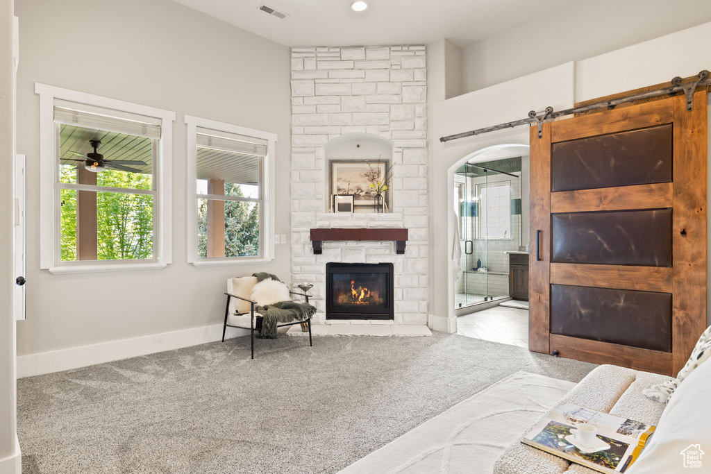 Carpeted living area with a fireplace, baseboards, a barn door, and a ceiling fan