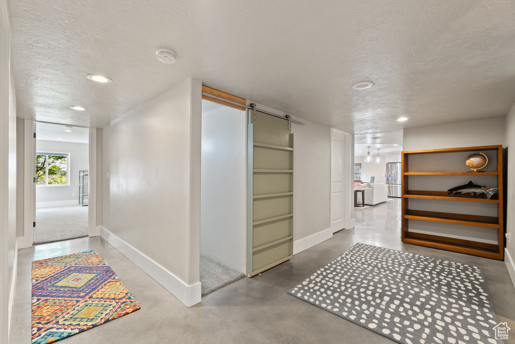 Hallway with a textured ceiling, baseboards, concrete flooring, a barn door, and recessed lighting
