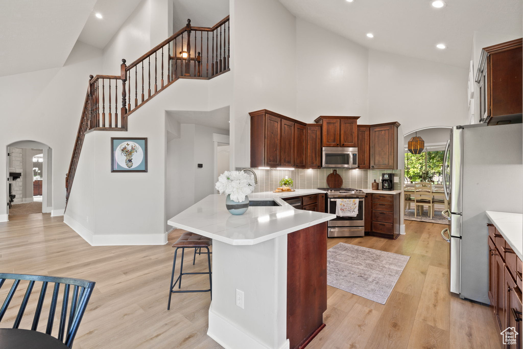 Kitchen featuring appliances with stainless steel finishes, arched walkways, high vaulted ceiling, a sink, and a peninsula