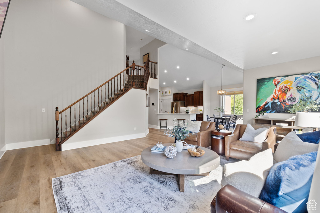 Living room featuring stairs, light wood-type flooring, baseboards, recessed lighting, and lofted ceiling