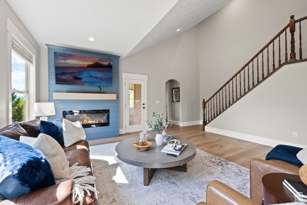 Living room featuring arched walkways, vaulted ceiling, wood finished floors, baseboards, and a fireplace