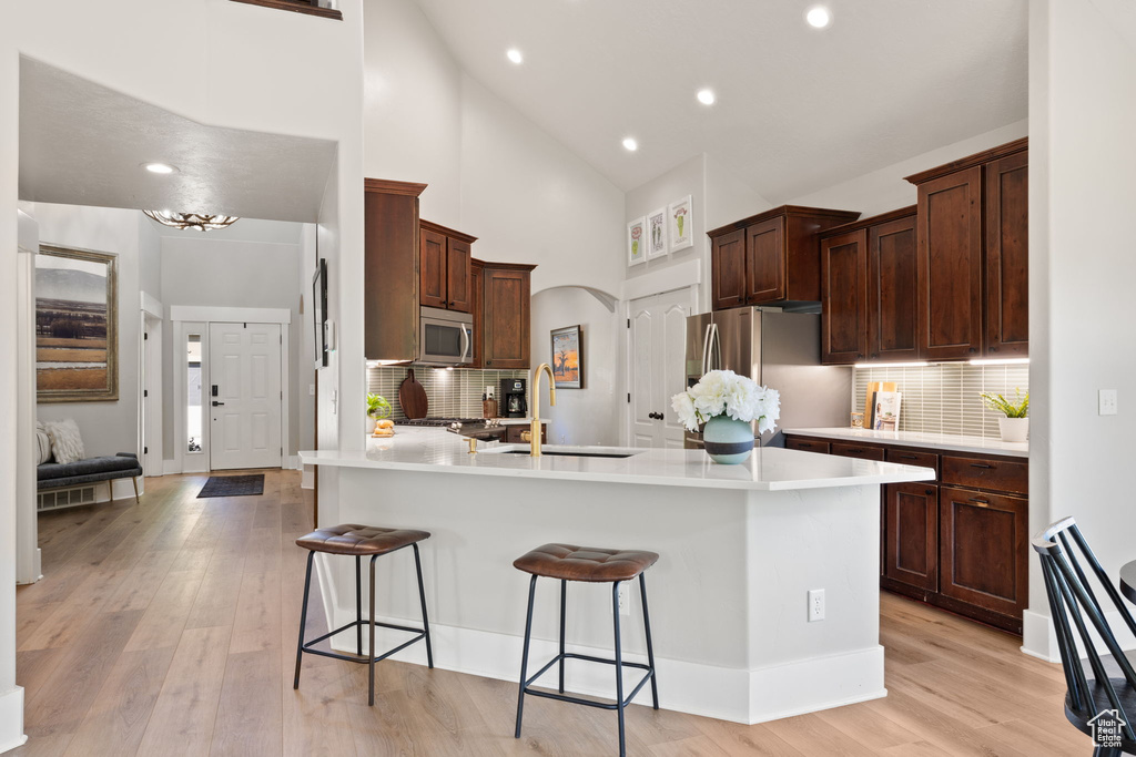 Kitchen featuring a sink, stainless steel appliances, a breakfast bar, backsplash, and high vaulted ceiling