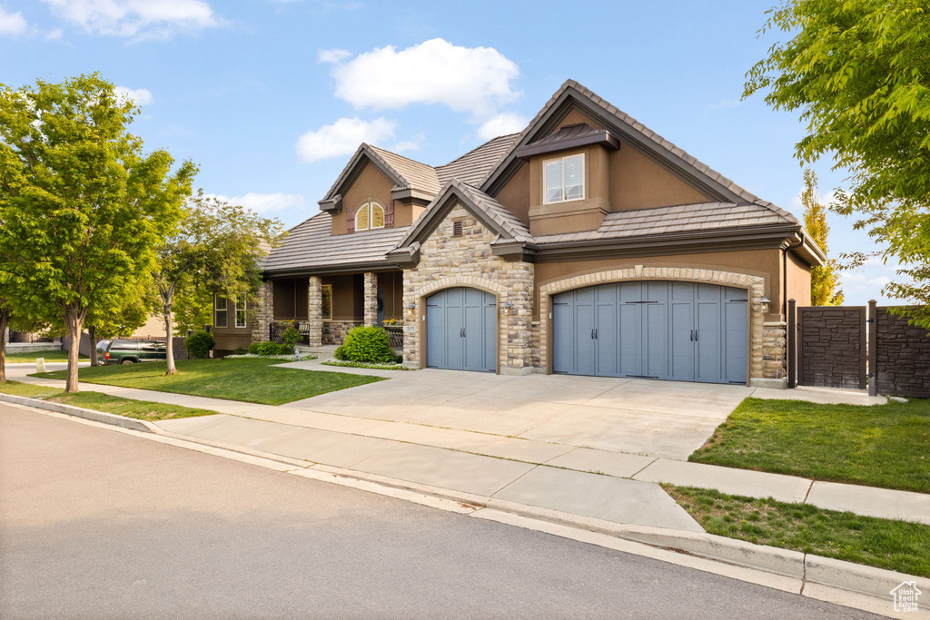 View of front of house featuring stone siding, concrete driveway, stucco siding, covered porch, and a tiled roof