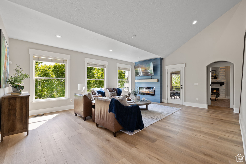 Living area with a glass covered fireplace, light wood-style floors, arched walkways, recessed lighting, and high vaulted ceiling