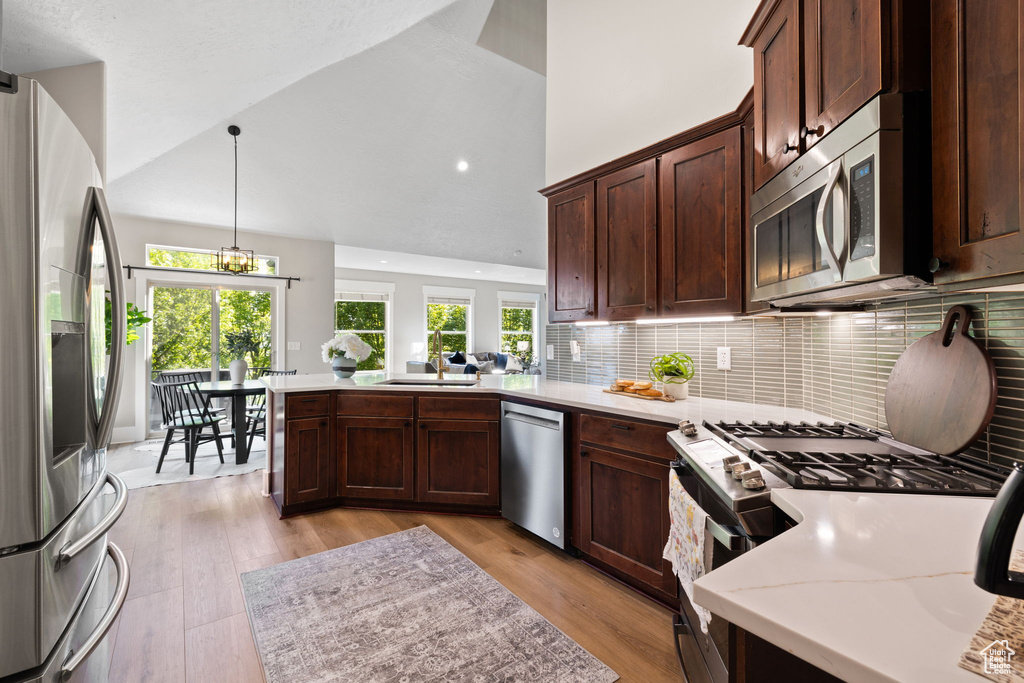 Kitchen featuring appliances with stainless steel finishes, a sink, a peninsula, light wood-style flooring, and high vaulted ceiling