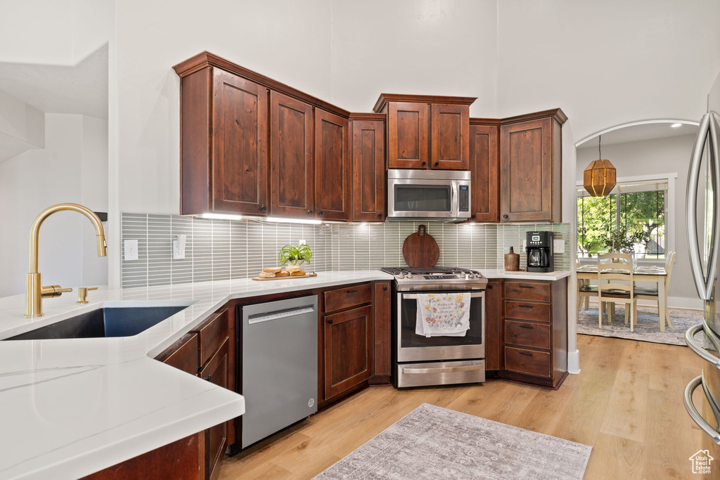 Kitchen featuring appliances with stainless steel finishes, a sink, light countertops, light wood finished floors, and backsplash