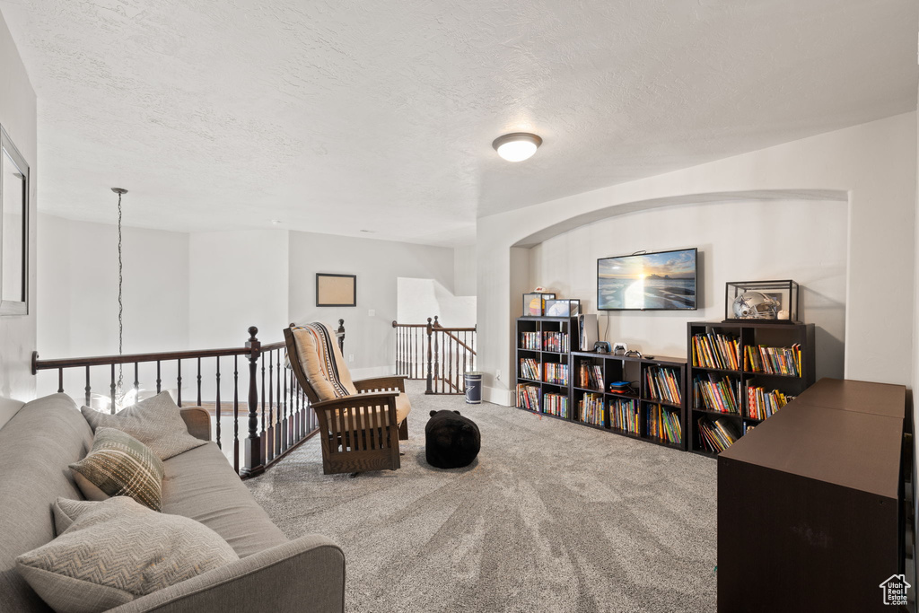 Living area featuring an upstairs landing, carpet, a textured ceiling, and arched walkways