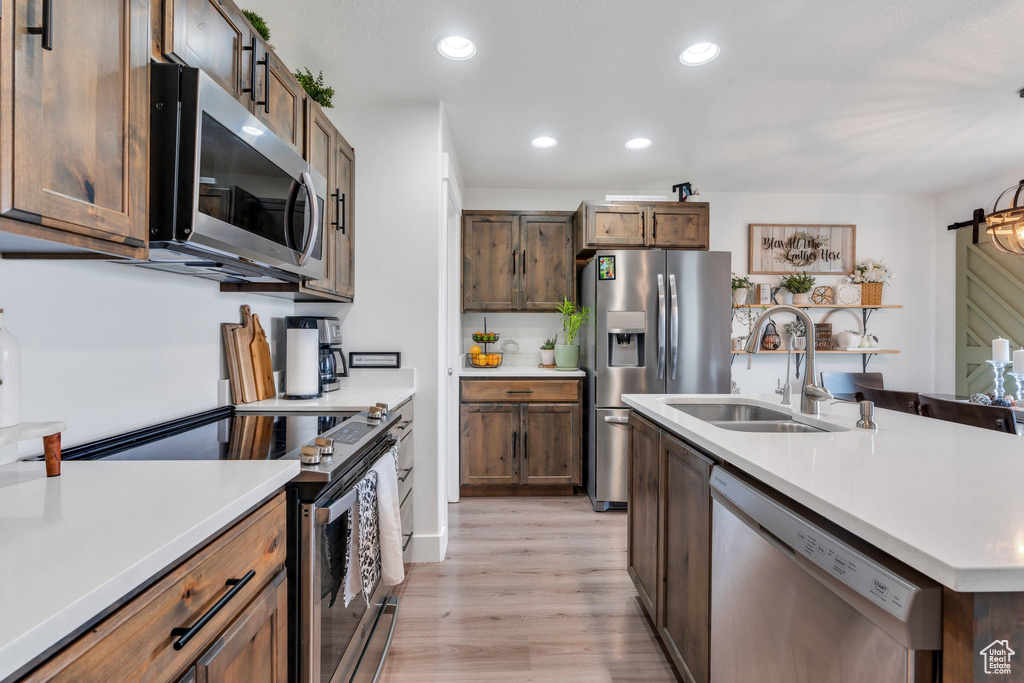 Kitchen with stainless steel appliances, a sink, light wood-type flooring, light countertops, and recessed lighting