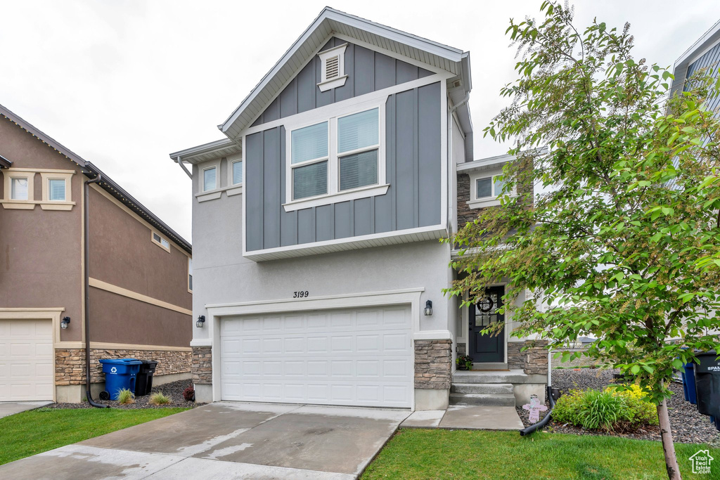 View of front of house featuring stone siding, board and batten siding, an attached garage, and driveway