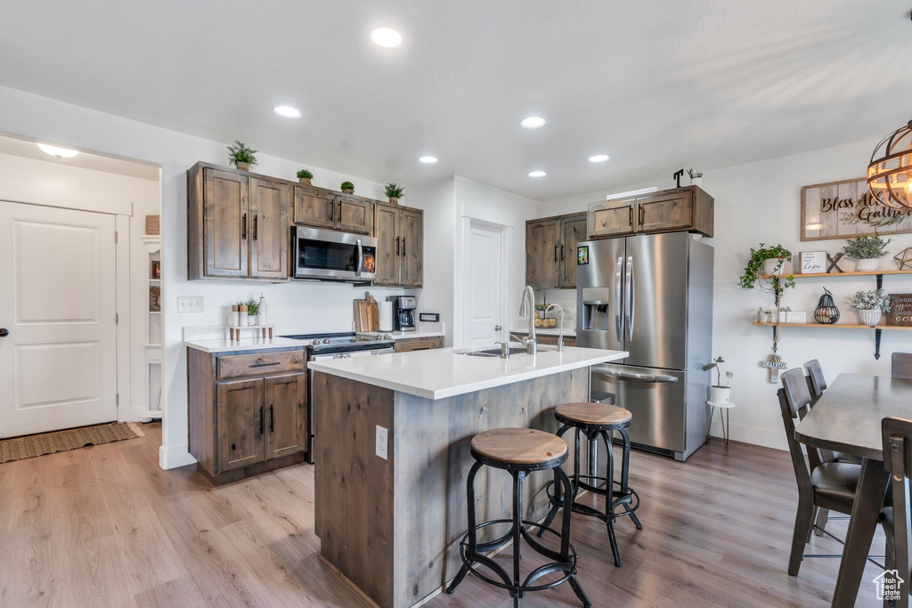 Kitchen featuring stainless steel appliances, a sink, a breakfast bar, light countertops, and recessed lighting