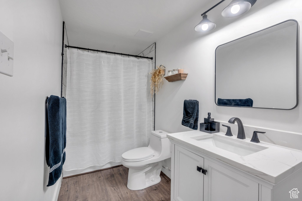 Full bath with toilet, vanity, wood finished floors, and curtained shower