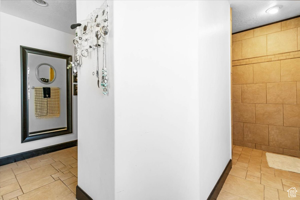 Corridor with a textured ceiling, baseboards, and tile walls