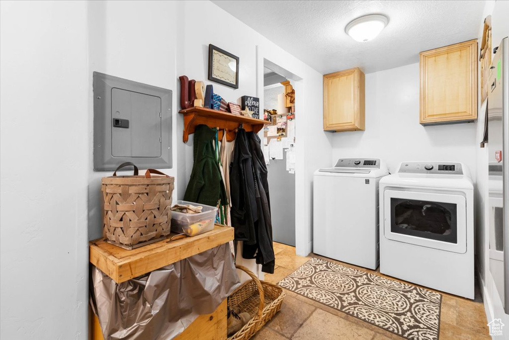 Clothes washing area with washer and dryer, electric panel, cabinet space, and a textured ceiling