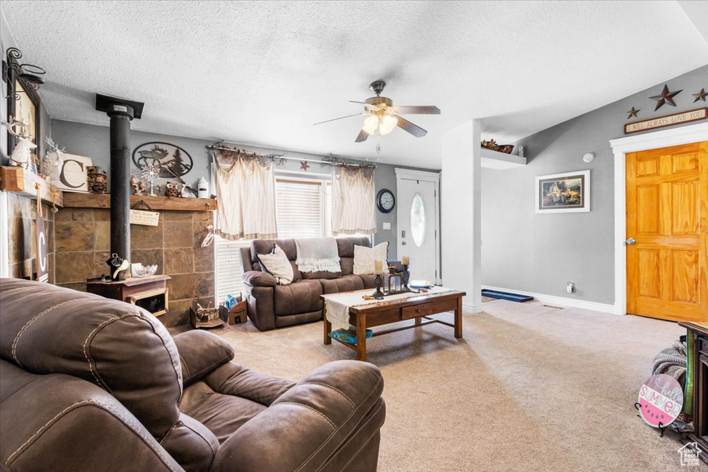 Carpeted living room with a wood stove, a ceiling fan, a textured ceiling, and baseboards