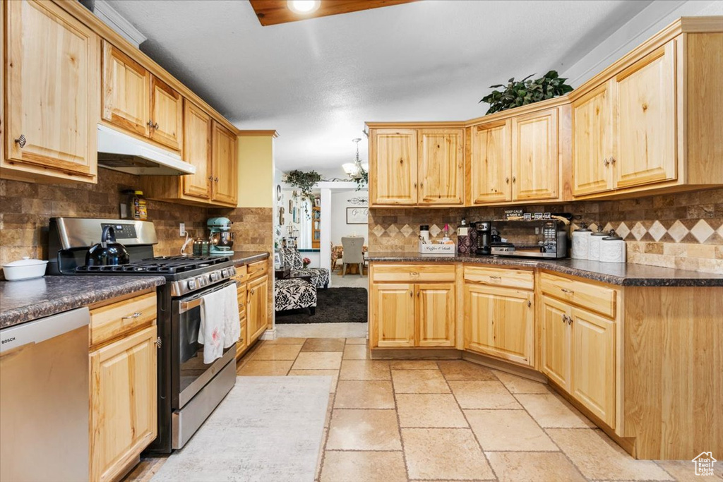 Kitchen with stainless steel appliances, under cabinet range hood, dark countertops, backsplash, and light brown cabinetry