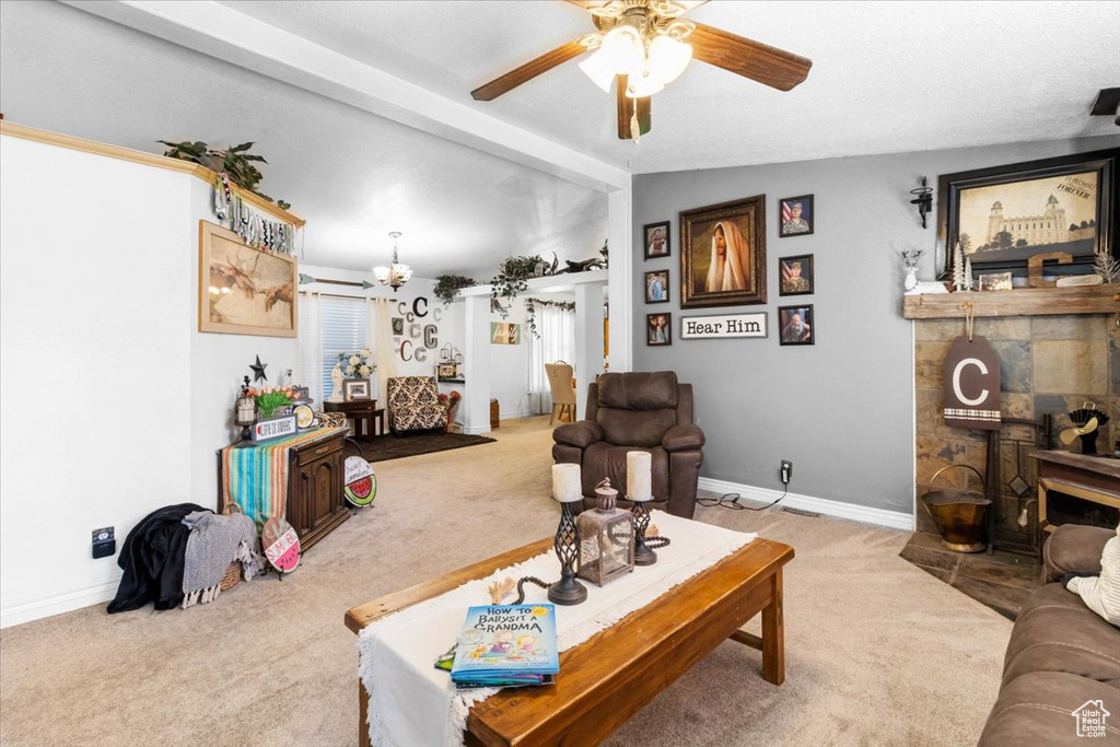 Carpeted living area featuring ceiling fan, a fireplace, baseboards, and a chandelier