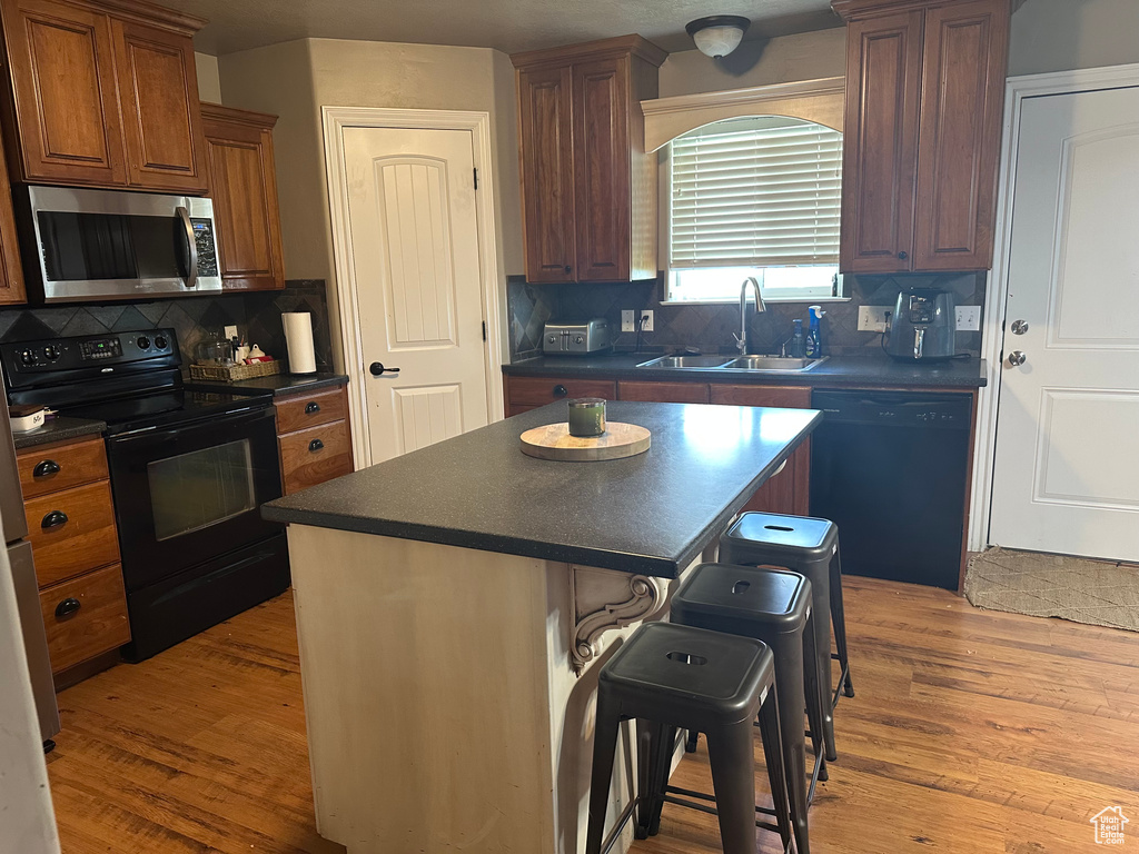 Kitchen featuring black appliances, a sink, dark countertops, and a breakfast bar area