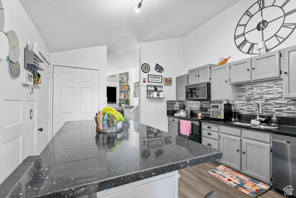 Kitchen featuring stainless steel appliances, a sink, decorative backsplash, wood finished floors, and dark stone counters
