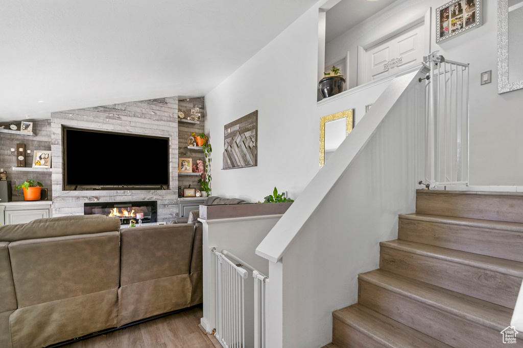 Stairway with vaulted ceiling, wood finished floors, and a glass covered fireplace