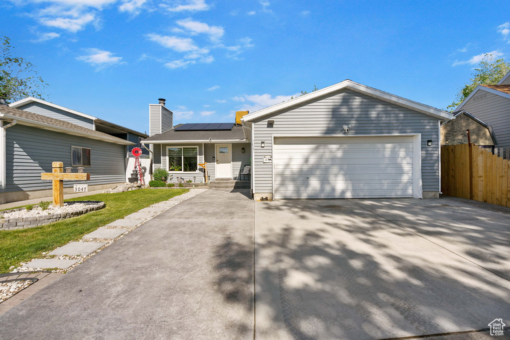 Ranch-style house with fence, solar panels, driveway, and a garage