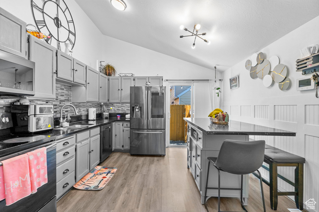 Kitchen with stainless steel appliances, a sink, gray cabinets, dark countertops, and lofted ceiling