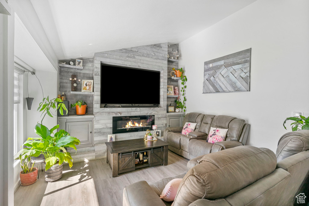 Living area with vaulted ceiling, wood finished floors, and a stone fireplace