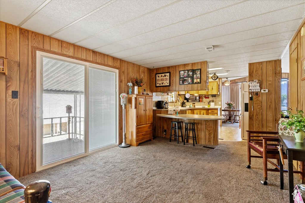 Kitchen with wooden walls, light colored carpet, brown cabinetry, light countertops, and stainless steel microwave