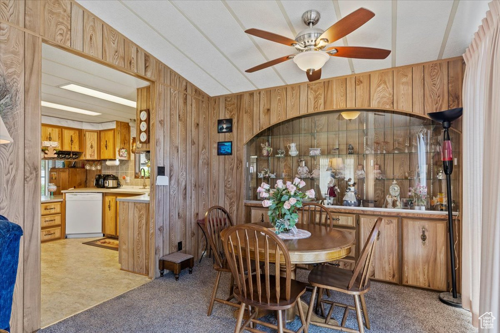 Dining space featuring wood walls, a ceiling fan, and light carpet