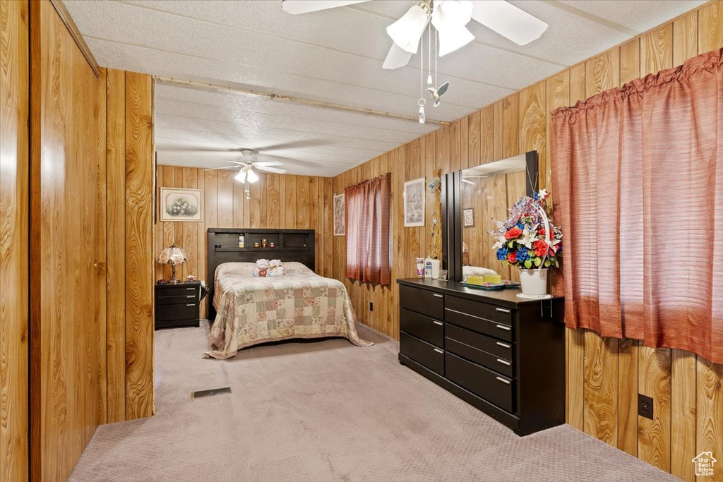 Carpeted bedroom with wood walls and a ceiling fan