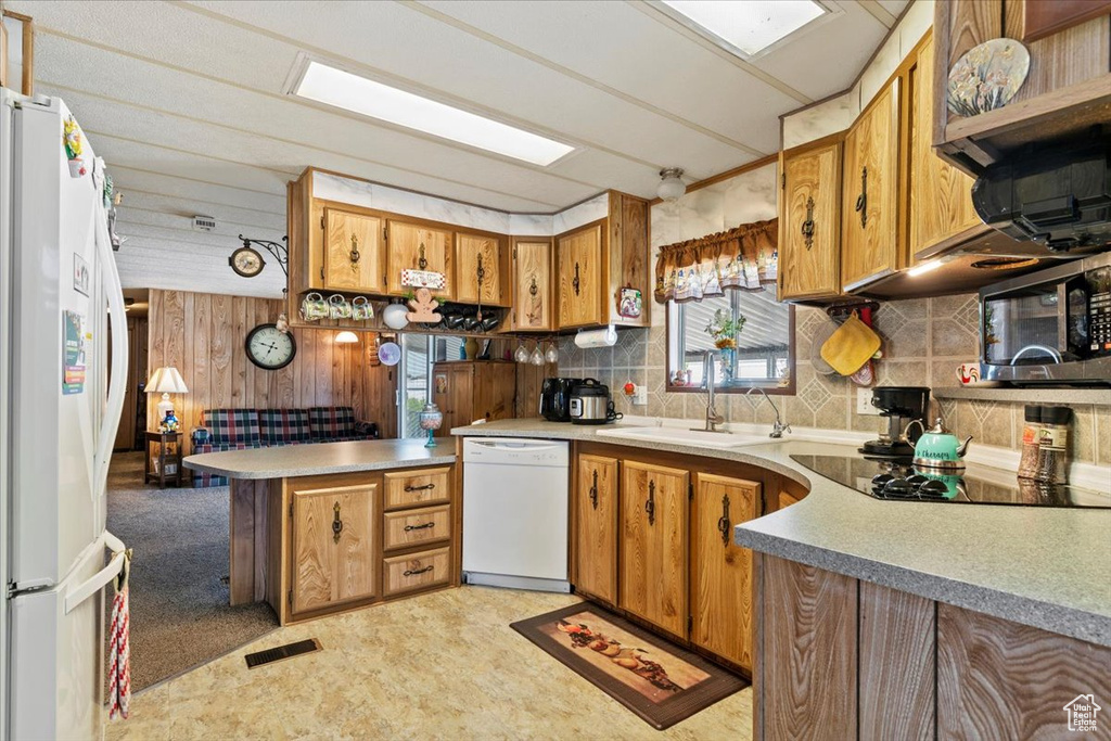 Kitchen with white appliances, a sink, a peninsula, brown cabinets, and wooden walls