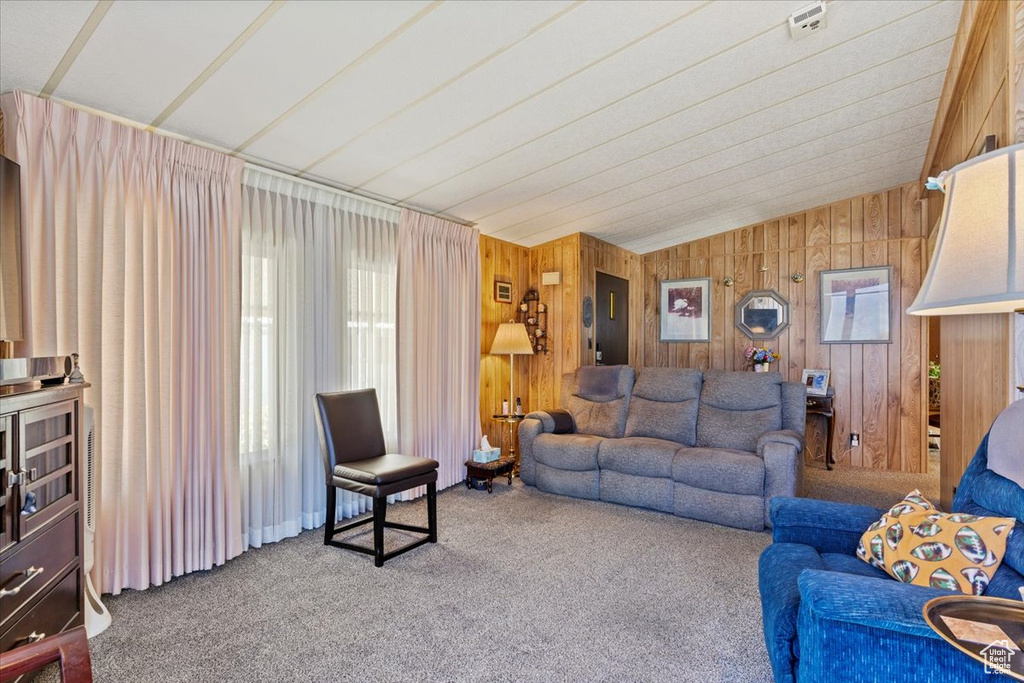 Living room featuring carpet, plenty of natural light, wooden walls, and vaulted ceiling