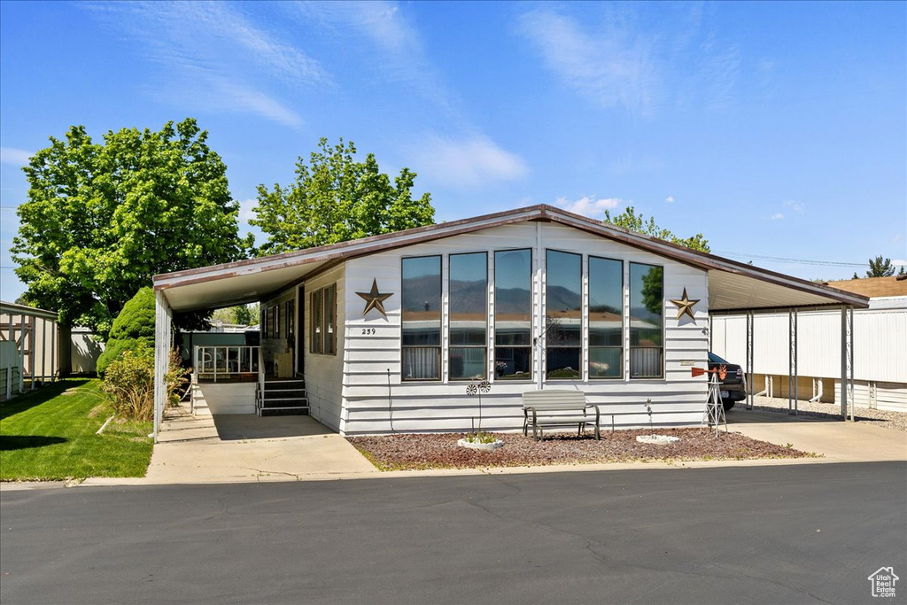 Manufactured / mobile home featuring an attached carport, driveway, and fence