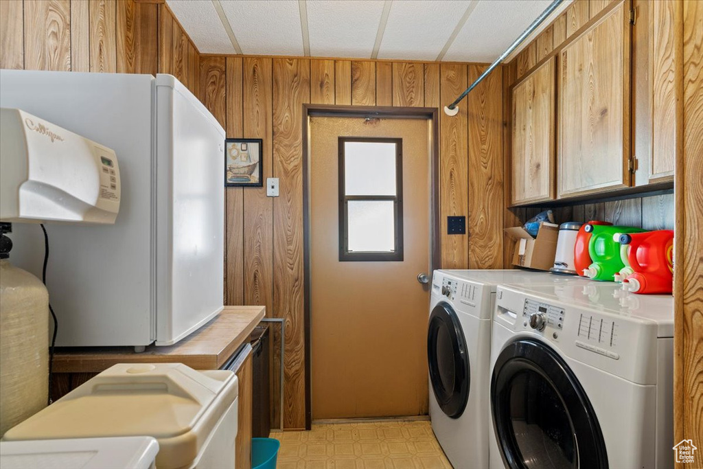 Washroom with washer and dryer, wooden walls, light floors, and cabinet space