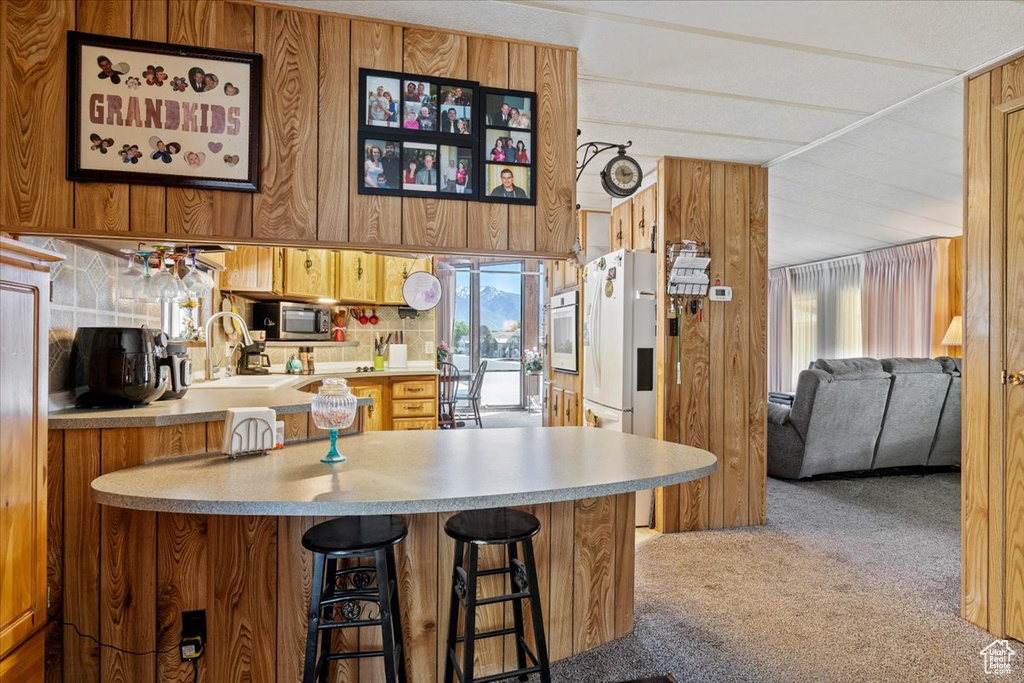 Kitchen with white appliances, light colored carpet, a sink, light countertops, and a kitchen bar