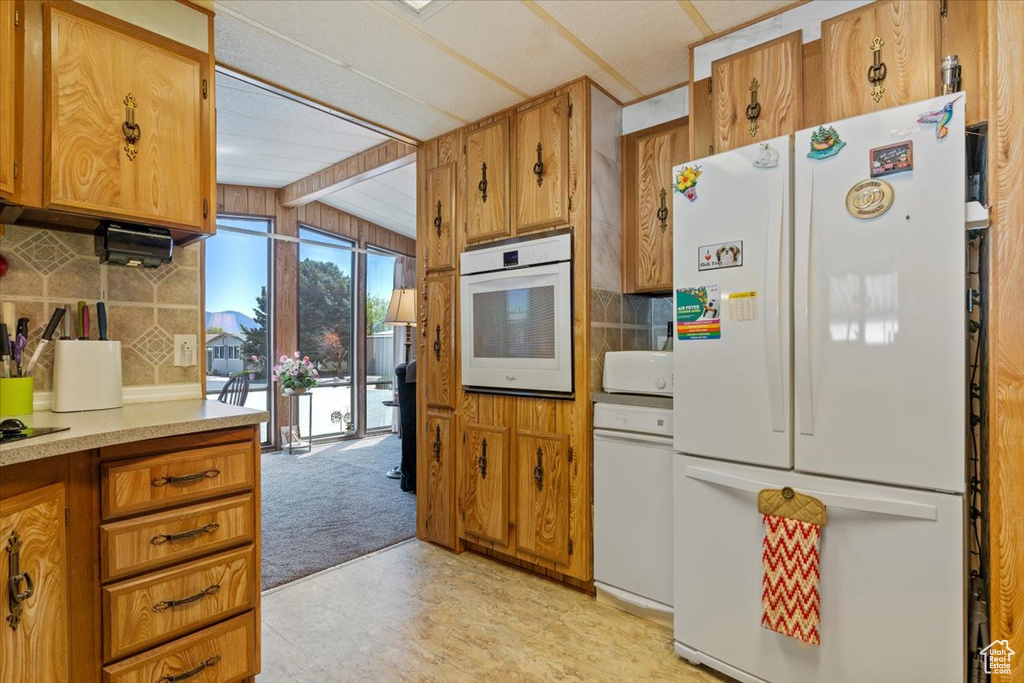 Kitchen featuring white appliances, decorative backsplash, light countertops, and brown cabinetry