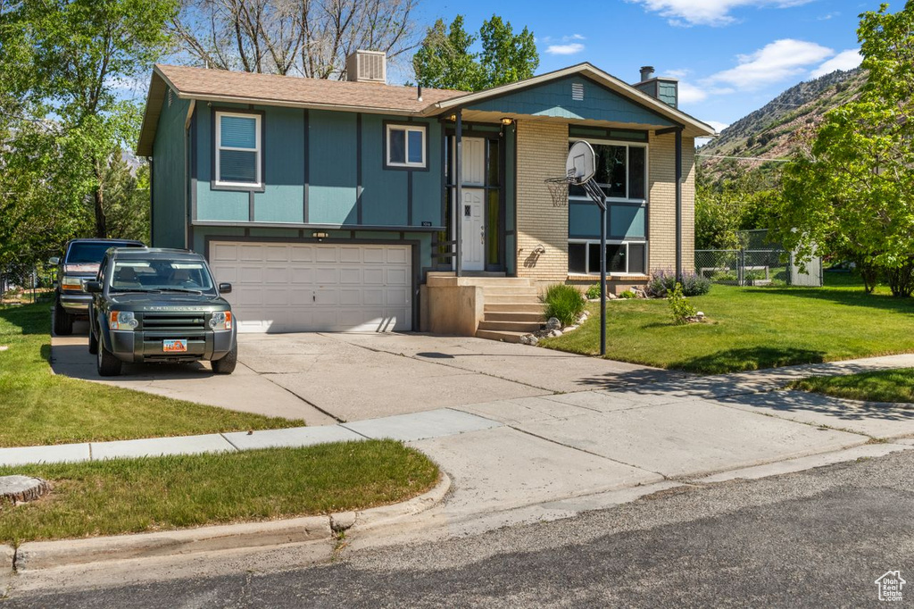 Raised ranch with a chimney, concrete driveway, a garage, a front yard, and a mountain view