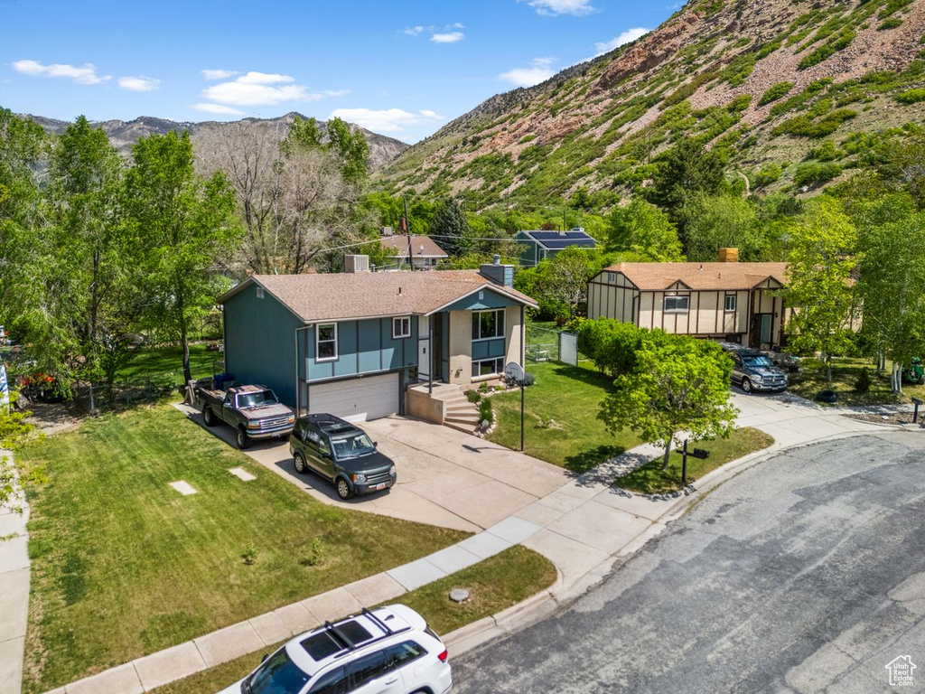 Ranch-style home with concrete driveway, a garage, a mountain view, a chimney, and a front yard