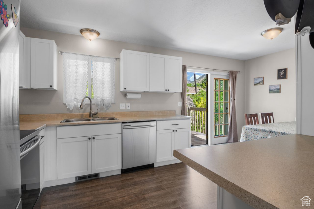 Kitchen featuring stainless steel appliances, a sink, dark wood finished floors, and white cabinetry