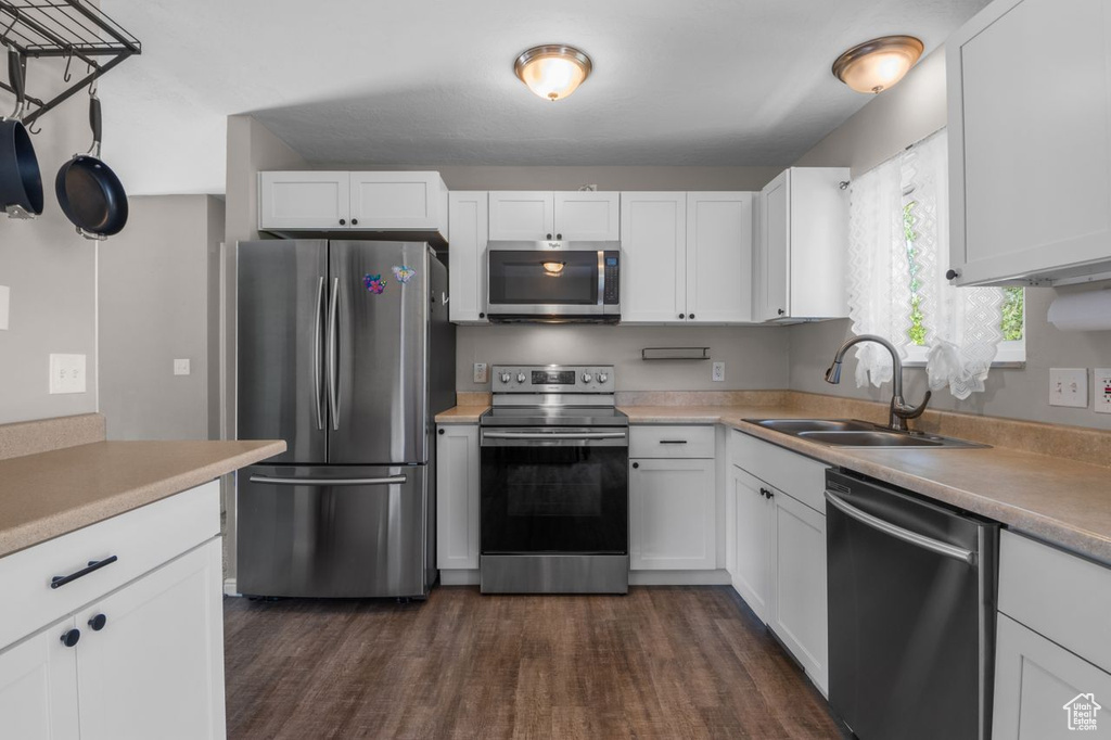 Kitchen with appliances with stainless steel finishes, a sink, dark wood finished floors, white cabinetry, and light countertops