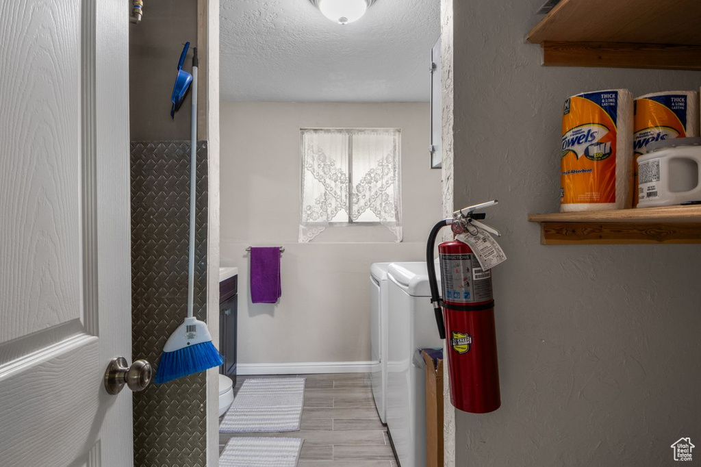 Laundry room with washing machine and dryer, a textured ceiling, baseboards, and a textured wall