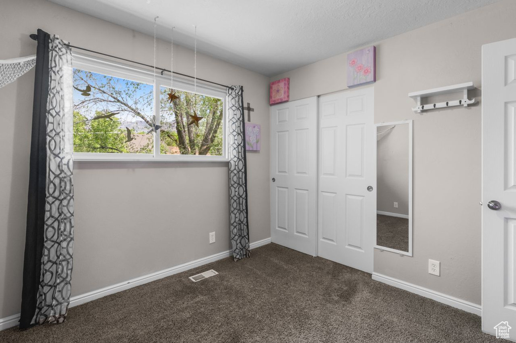 Unfurnished bedroom with dark colored carpet, a closet, and baseboards