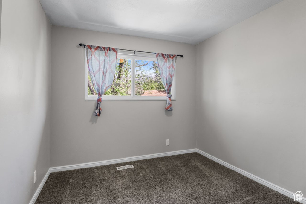 Unfurnished room featuring dark carpet and baseboards