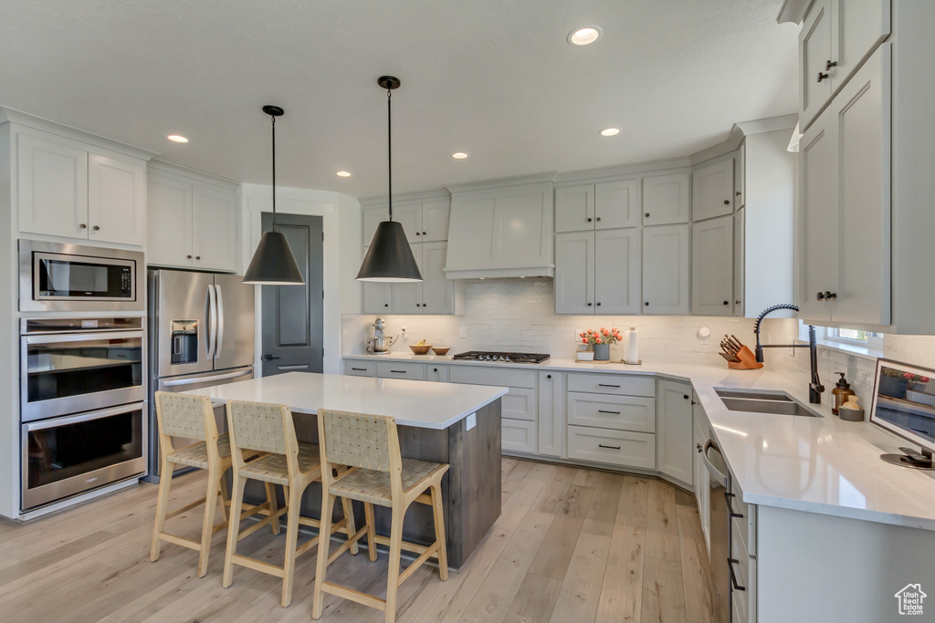 Kitchen with stainless steel appliances, a sink, light wood-style flooring, light countertops, and recessed lighting