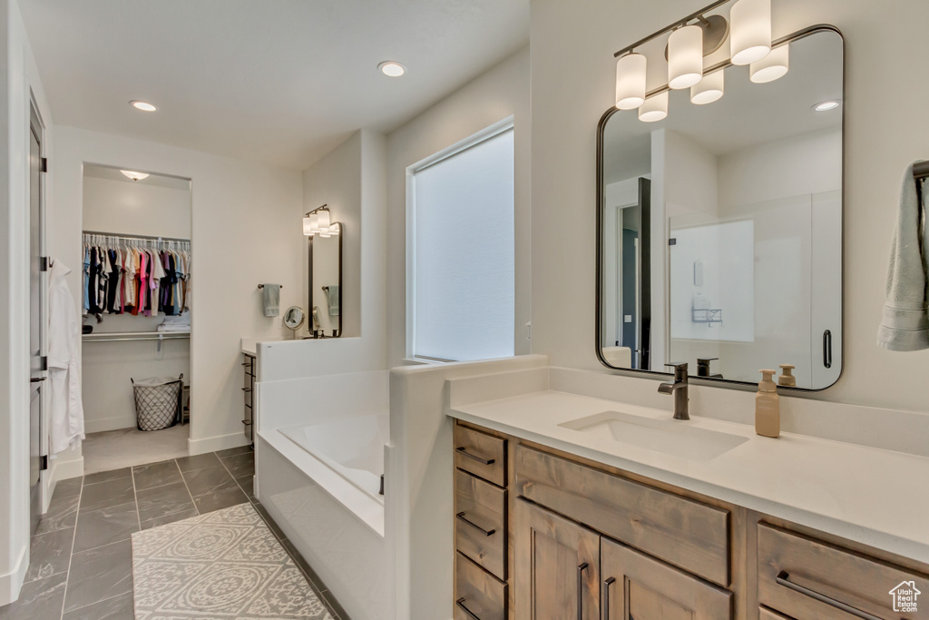 Bathroom with a garden tub, recessed lighting, a spacious closet, vanity, and marble look tiles